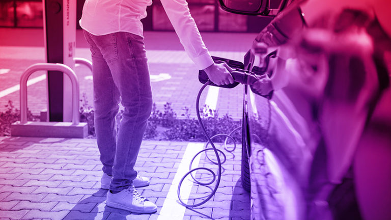 Elektroauto Laden auf Parkplatz, Mann mit Hand am Stecker