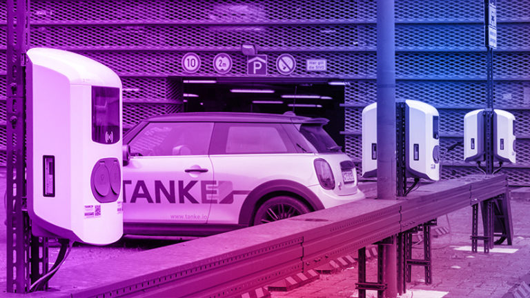 TankE Auto steht an Wallbox auf einem Parkplatz vor Parkhaus